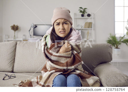 Young woman freezing in her house in winter due to some problems with central heating Young woman freezing in her house in winter due to some problems with central heating 128758764