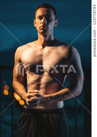 Muscular athlete posing powerfully at night, strength and dedication, Toned man with perfect body displaying power and discipline in evening silhouette 128758784