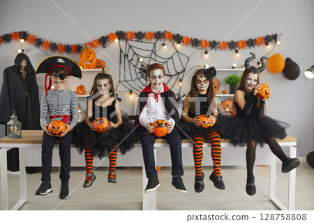 Children dressed in various spooky characters sit in row holding pumpkin buckets for candy. 128758808
