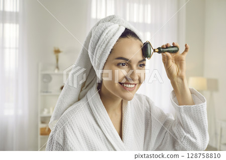 Woman massaging face with facial roller for lymphatic drainage and blood circulation 128758810