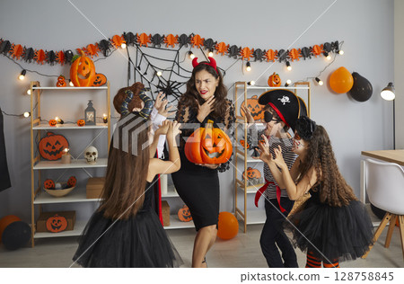 Group of children in spooky costumes trying to scare their teacher at Halloween party 128758845