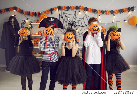 Children group in masquerade costumes pose with pumpkins 128758888