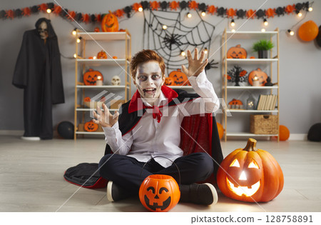 Portrait of boy dressed up as scary vampire for Halloween night sitting on floor at home 128758891