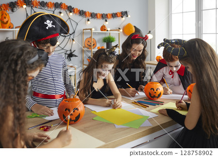 Arts and Crafts teacher and children dressed up in costumes having fun class on Halloween 128758902