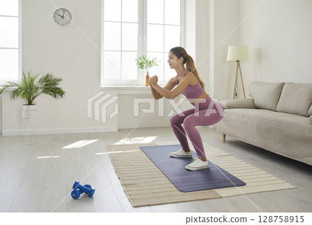 Happy fit young woman in sportswear doing squats during a fitness workout at home 128758915