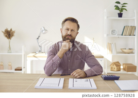 Portrait of focused pensive businessman looking at camera while sitting in office. 128758928