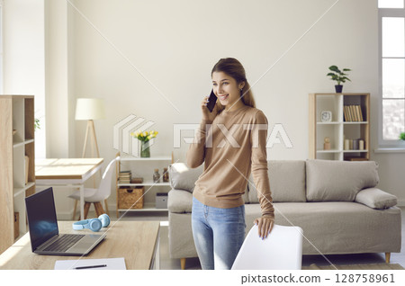 Young female business owner dropshipping at home talking on mobile phone and taking orders. Young female business owner dropshipping at home talking on mobile phone and taking orders. 128758961