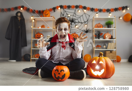 Terrifying child in traditional Halloween vampire costume who screams and scares looking at camera. 128758980
