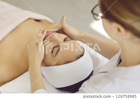 Young woman getting beauty treatments and facial massage while relaxing at spa salon Young woman getting beauty treatments and facial massage while relaxing at spa salon 128758985