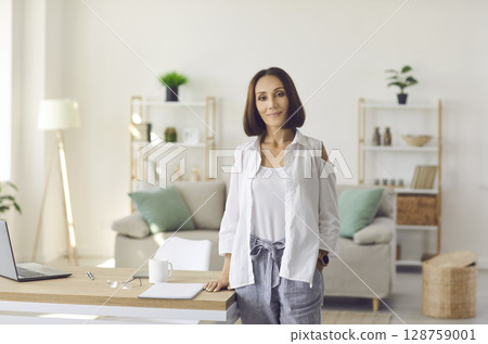 Portrait of confident middle-aged business woman standing in her cozy home office. 128759001