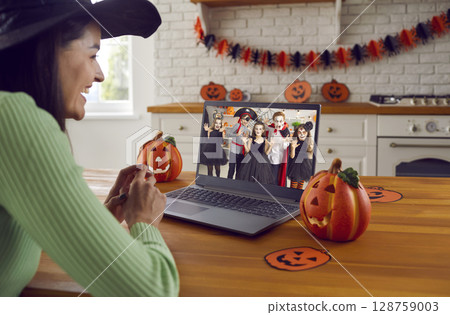 Happy woman in front of computer screen having online Halloween party with children 128759003