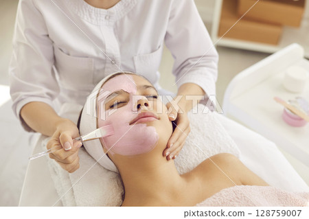 Young woman or teen girl enjoying cosmetic clay facial mask in spa and beauty salon 128759007