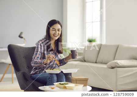 Happy woman drinking coffee and eating vegetable salad from takeout meal delivery Happy woman drinking coffee and eating vegetable salad from takeout meal delivery 128759009