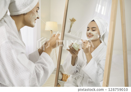 Young woman look in mirror do face mask Young woman look in mirror do face mask 128759010