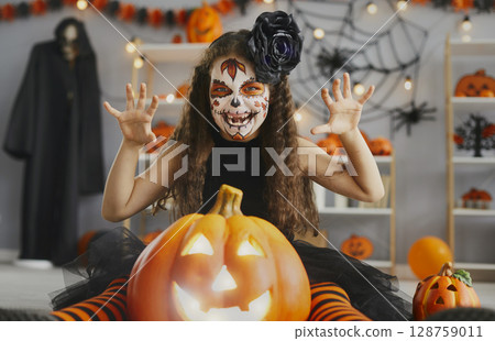 Portrait of a little girl in a spooky costume and skull makeup at a Halloween party 128759011