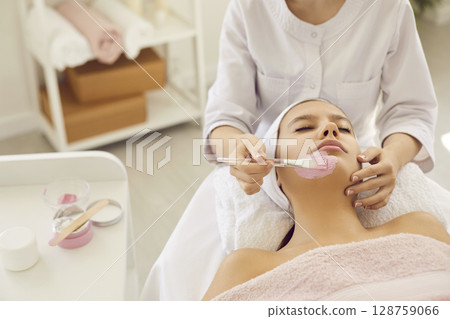 Relaxed young woman enjoying cosmetic pink clay facial mask in beauty or spa salon Relaxed young woman enjoying cosmetic pink clay facial mask in beauty or spa salon 128759066