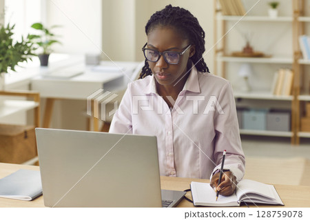 Portrait of african american business woman working on a laptop at office. 128759078