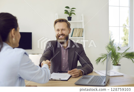 Businessman shakes hands with candidate during interview and congratulates her on getting new job. 128759103