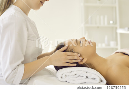 Happy relaxed young woman getting cosmetic facial treatment at beauty and spa salon Happy relaxed young woman getting cosmetic facial treatment at beauty and spa salon 128759253