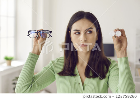 Young woman holding glasses and eye lenses and hesitating which solution to choose 128759260