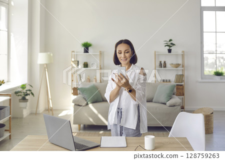 Portrait of stylish senior business woman standing with phone near workplace in her home office. 128759263