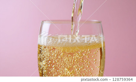 Pouring golden beverage into a glass with bubbles against a pink background creating a vibrant and refreshing look 128759364