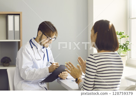 Male doctor writes prescription or makes notes in patient's card at medical examination. 128759379