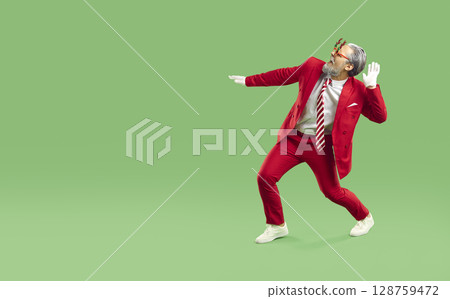 Horizontal shot of joyful man dressed in red suit like Santa Claus, dances and has fun 128759472