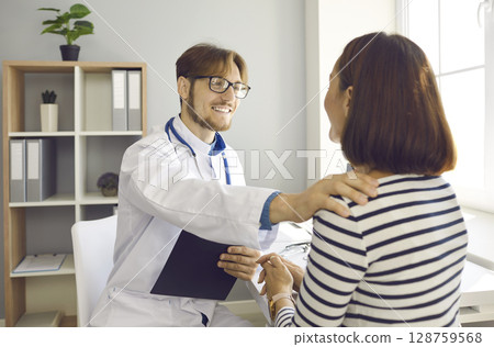 Smiling doctor talking to woman, touching her shoulder, supporting and reassuring her Smiling doctor talking to woman, touching her shoulder, supporting and reassuring her 128759568