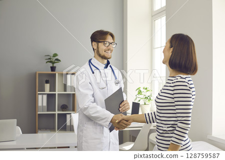 Male doctor shakes hands as sign of greeting and acquaintance with female patient at the hospital. 128759587