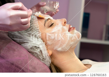 Therapist fans foamy facial mask onto client's cheek 128760163