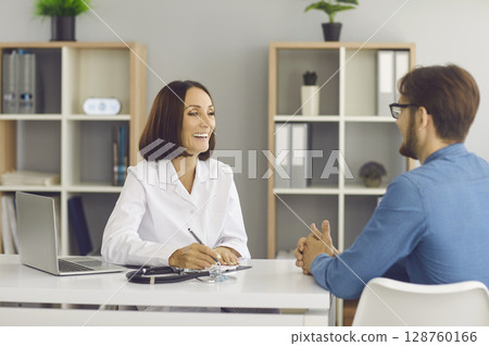 Cheerful female doctor advises her male patient during medical examination at hospital. Cheerful female doctor advises her male patient during medical examination at hospital. 128760166
