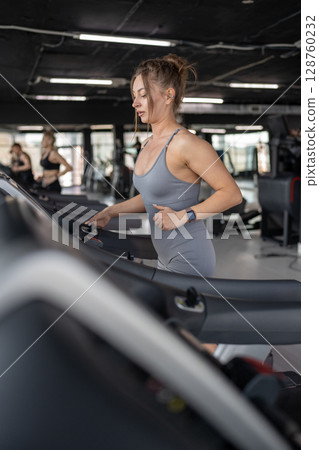 A young woman runs on a treadmill in a gym, showing her dedication to fitness and wellbeing 128760232