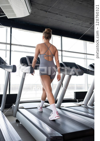 A fit woman confidently walking on a treadmill in a bright and inviting gym, promoting fitness and overall health. 128760321