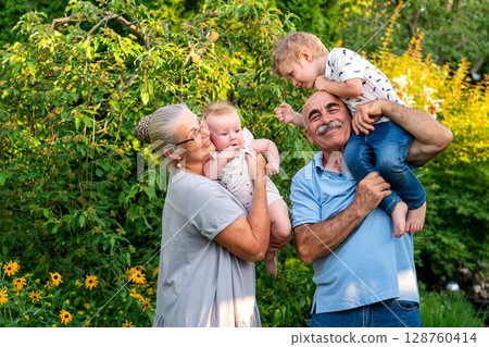 Grandparents smiling with two young grandchildren in garden 128760414