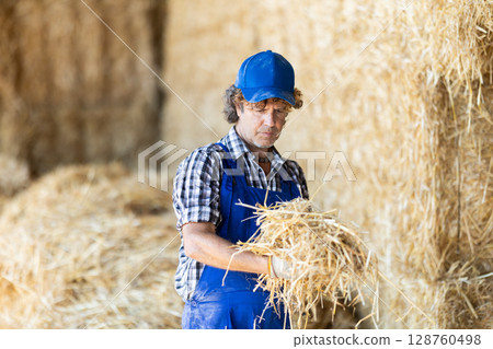 Male farmer checking straw in warehouse 128760498