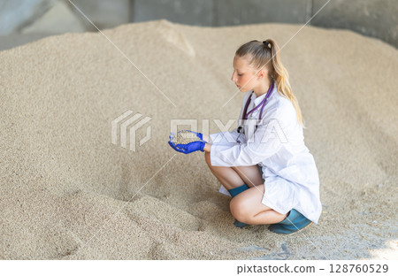 Young woman vet inspect granulated feed in storage 128760529