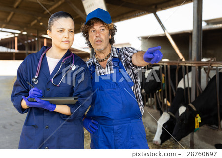 Man and Asian woman farmer with tablet talking at cowshed Man and Asian woman farmer with tablet talking at cowshed 128760697