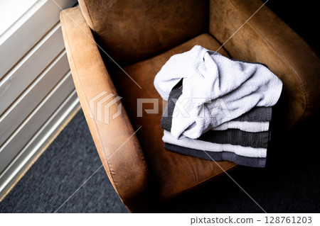Stack of clean towels on brown armchair in sunlit room corner Stack of clean towels on brown armchair in sunlit room corner 128761203
