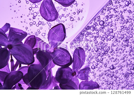 A petri dish with a beautiful serum texture on a purple background with lilac flowers. 128761499