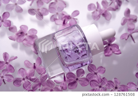 A bottle of serum with petals in water with lilac flowers. 128761508