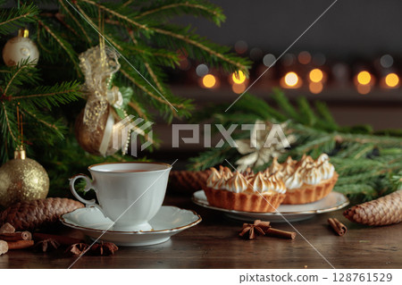 White cup of tea and meringue tartlet on table with Christmas decorations. 128761529