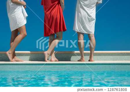 Group of individuals standing by a swimming pool, enjoying sunny day with clear blue sky 128761808