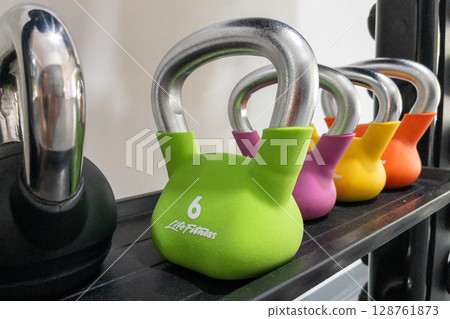 Colorful kettlebells arranged on gym rack for strength training and fitness workout. Colorful kettlebells arranged on gym rack for strength training and fitness workout. 128761873