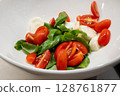 Caprese salad with cherry tomatoes, mozzarella and basil leaves in a white bowl. 128761877