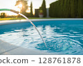 Water flowing from hose into swimming pool with sunlight reflecting on the surface 128761878