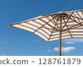 Striped beach umbrella against clear blue sky on a sunny day. 128761879