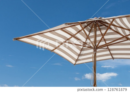 Striped beach umbrella against clear blue sky on a sunny day. 128761879