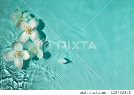 Blossoms on Water. White flowers floating on serene turquoise water with gentle ripples. 128762898