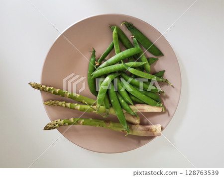 Heap of fresh peas and asparagus on a beige plate isolated on white background from a high angle view 128763539